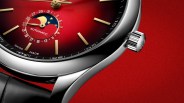 Close-up of a polished silver watch case with a red dial featuring gold hour markers, a moon phase indicator, and a black leather strap.