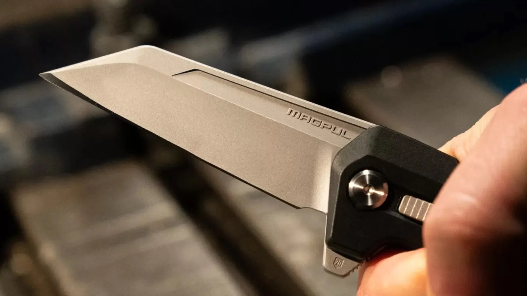 Close-up of a Magpul folding knife with a tan blade and black handle held in a hand.