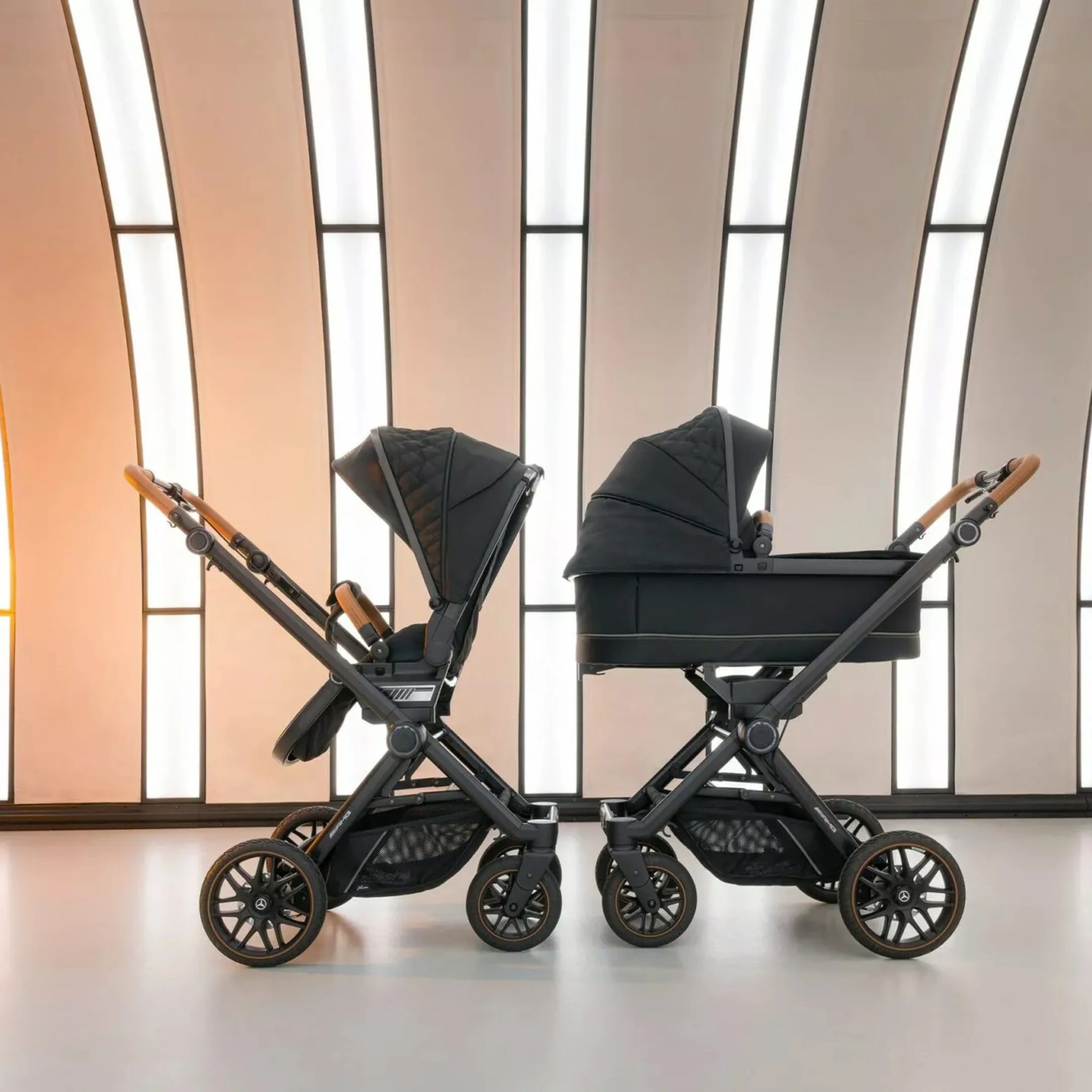 Two black baby strollers with brown handles, one with a seat and one with a bassinet, side by side indoors.