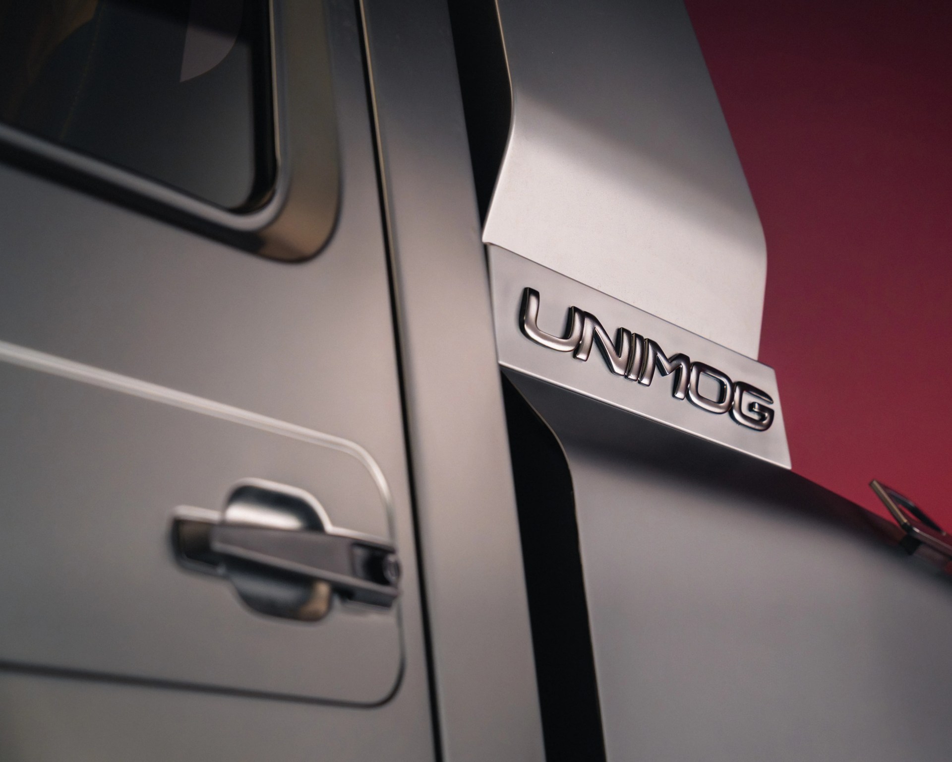 Close-up of a silver Unimog vehicle door and side panel with the Unimog logo on a metallic surface.