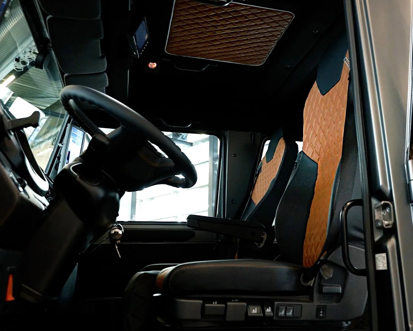 Black and tan diamond-stitched leather seats inside a vehicle cabin with a black steering wheel.