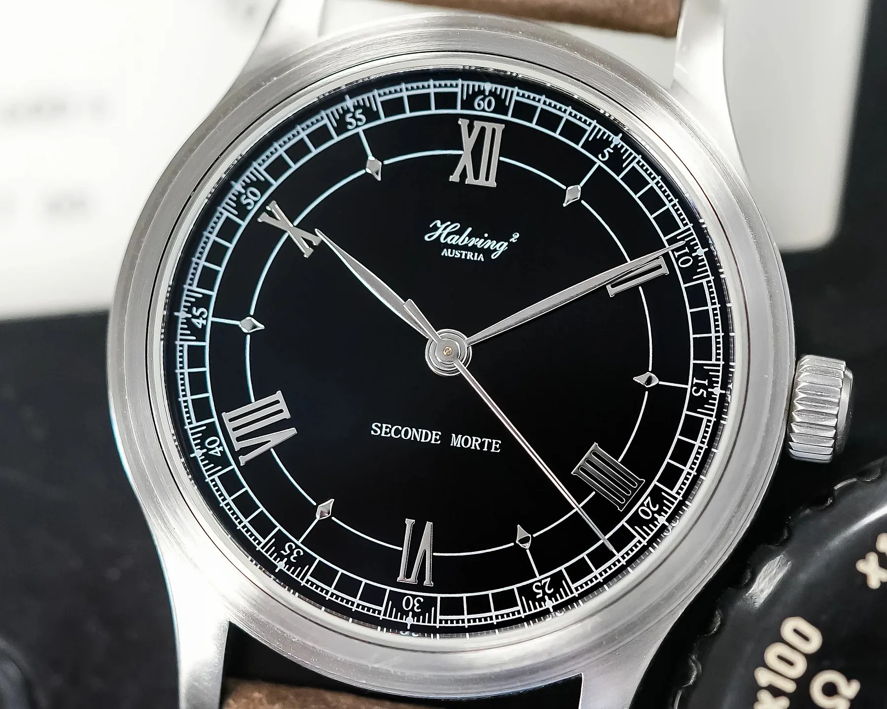 Close-up of a Habring&sup2; wristwatch with a black dial, silver Roman numerals, and silver hands showing 10:09:38.