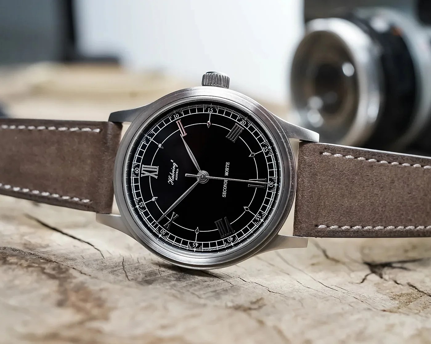 Silver wristwatch with black dial, Roman numerals, and brown leather strap on a wooden surface.
