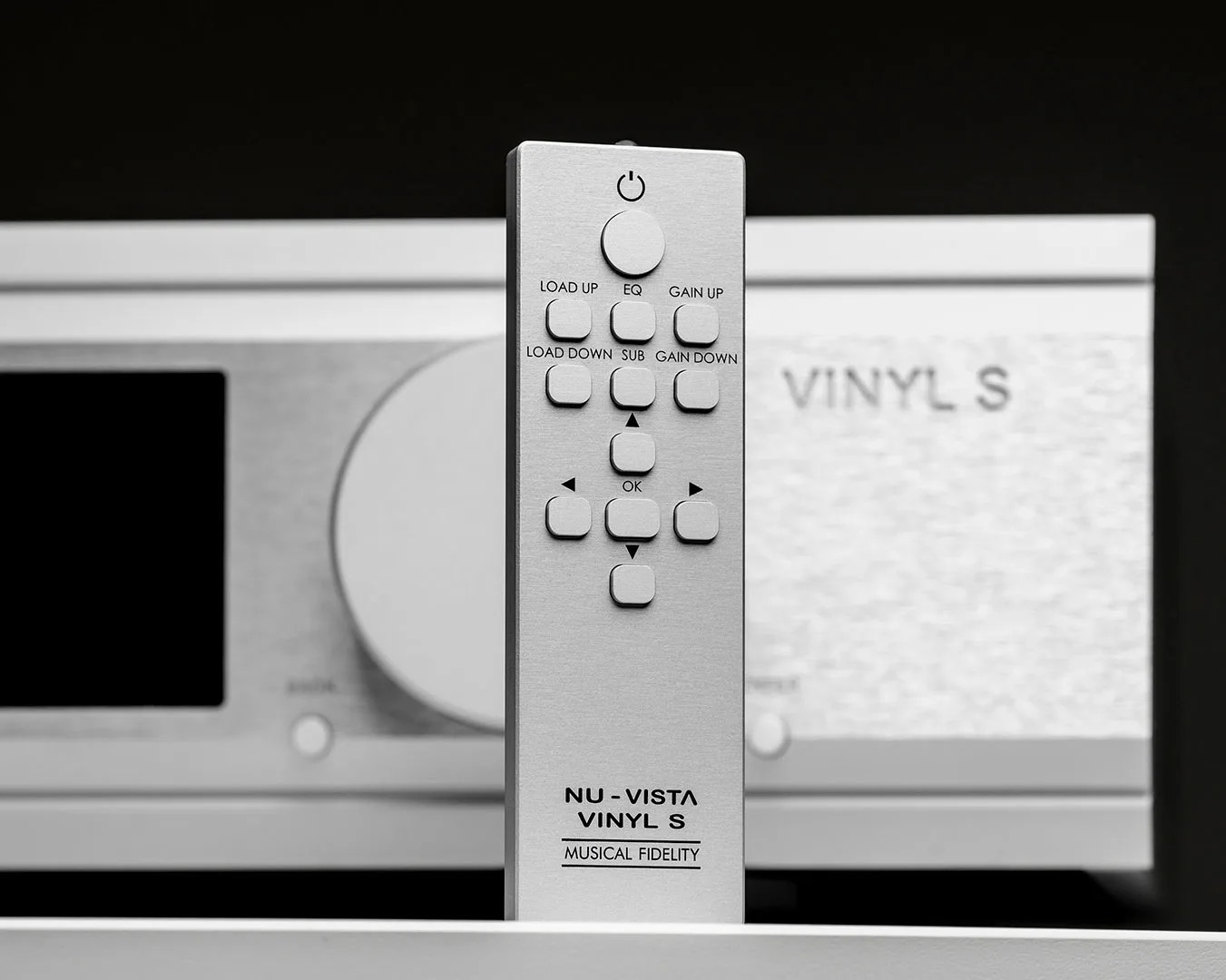 Silver remote control with buttons labeled for audio functions, standing in front of a matching silver audio device.