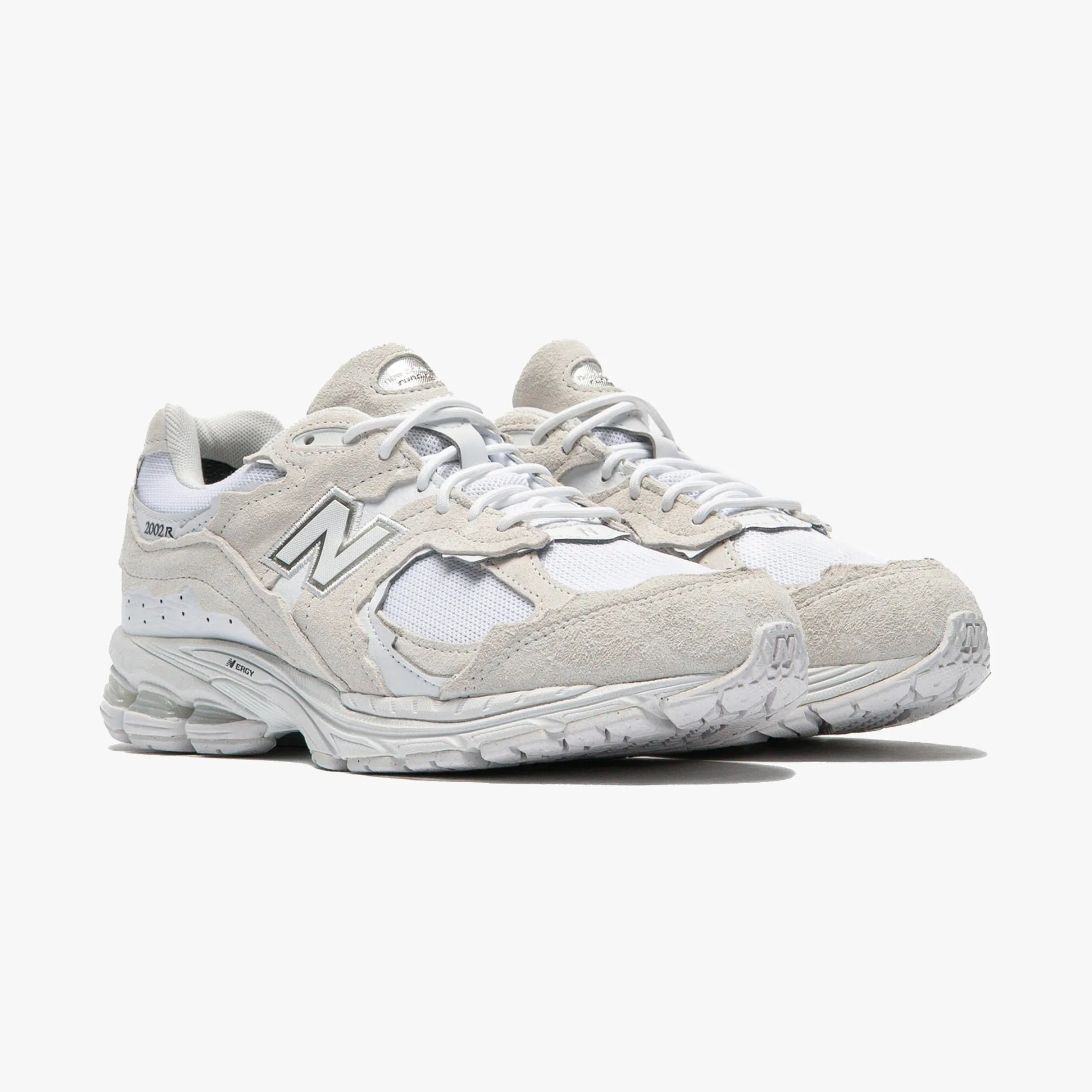 Pair of off-white New Balance 2002R sneakers with suede and mesh uppers and white laces on a white background.