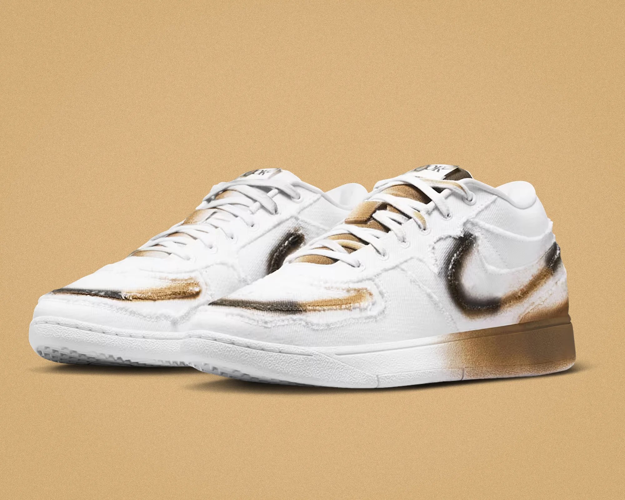 Pair of white low-top sneakers with brown and black spray paint accents on a tan background.