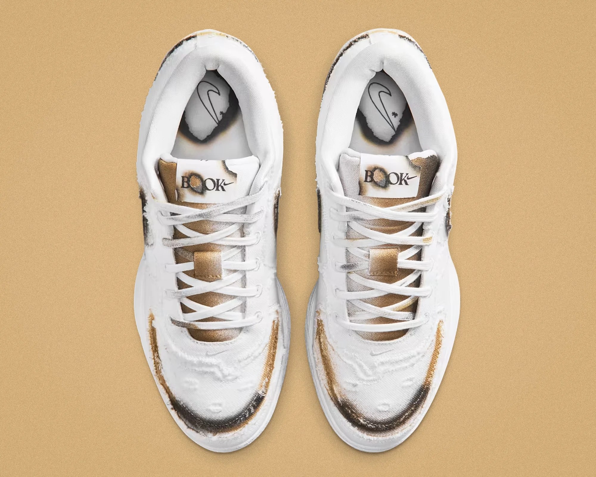Pair of white sneakers with distressed and burnt brown-black detailing on a tan background.
