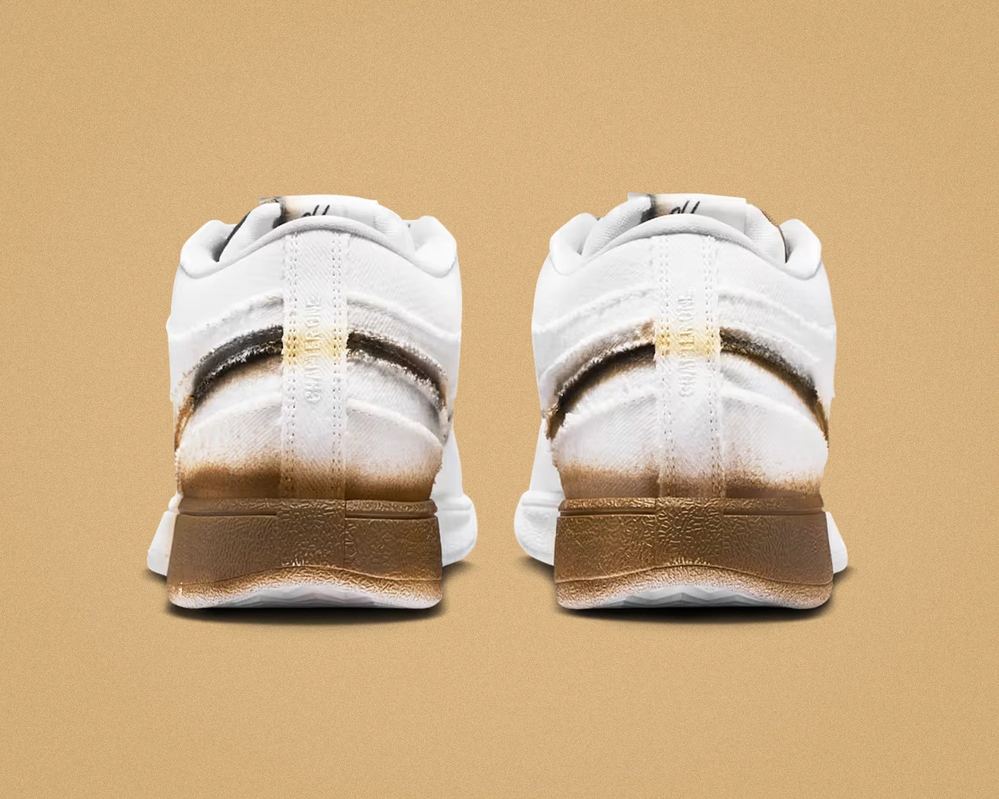 Pair of white sneakers with brown gradient soles and black and brown smudges on the back.
