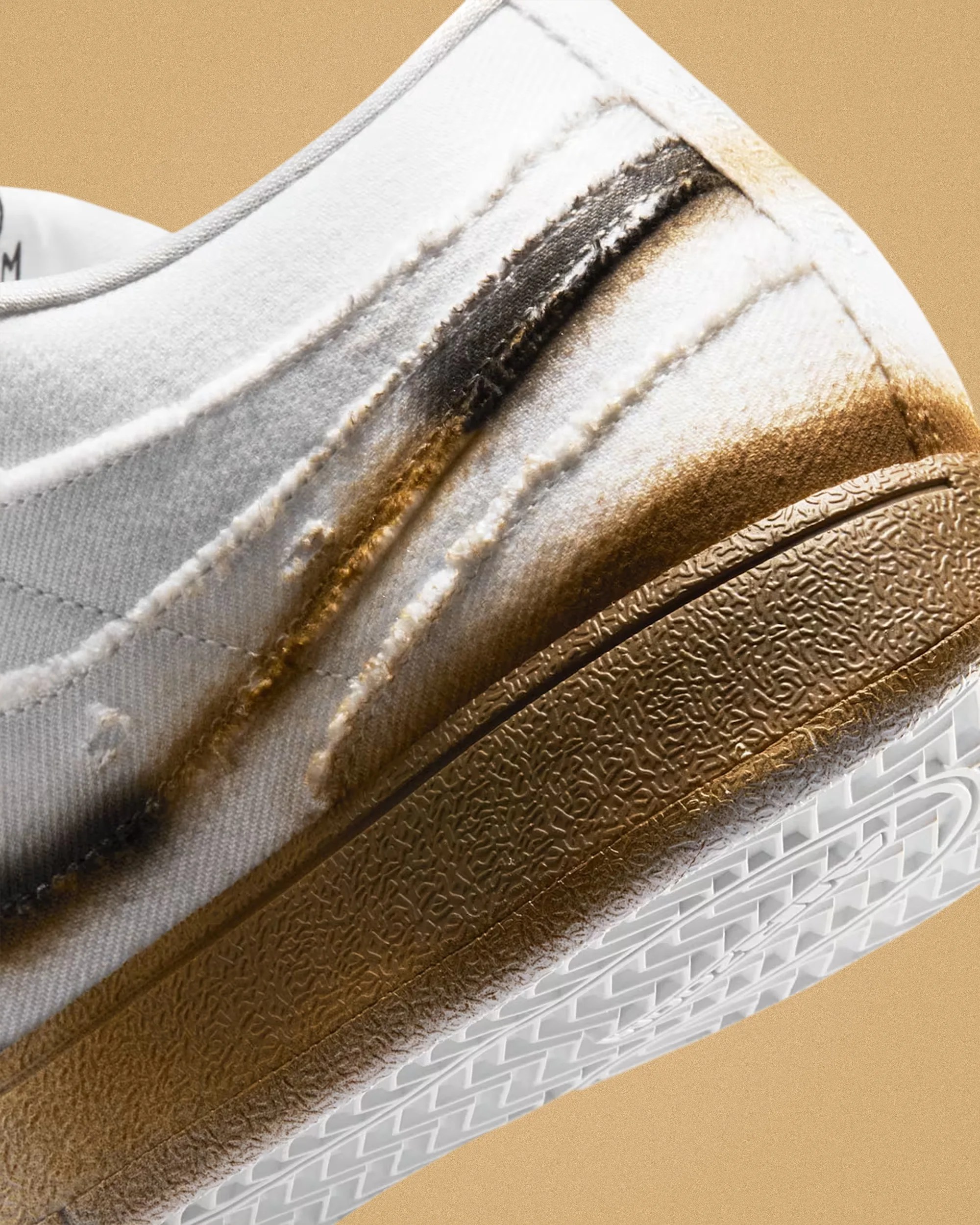Close-up of white sneaker with brown and black paint splatter on fabric upper and textured brown midsole.