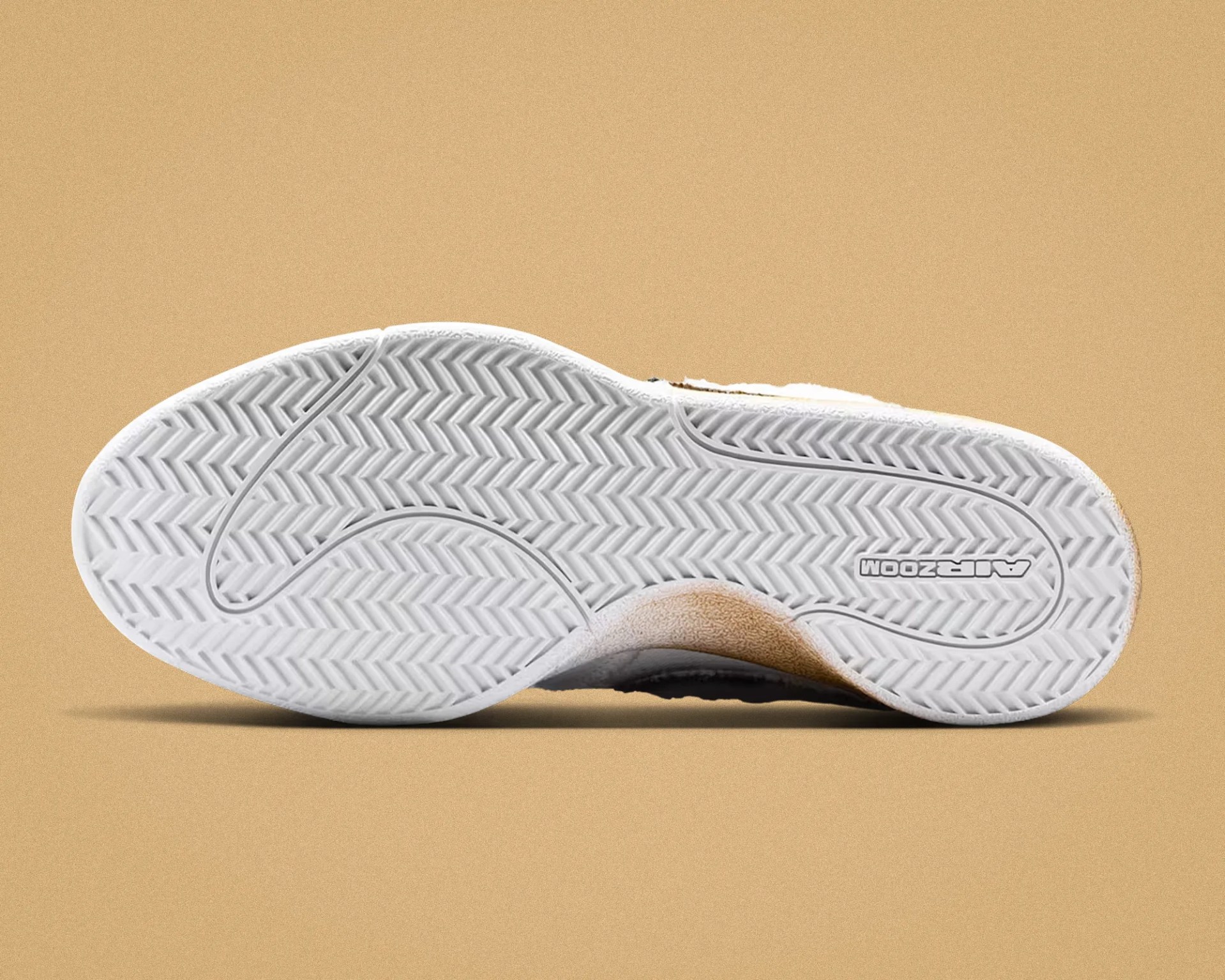 White rubber sole of a sneaker with herringbone tread pattern and "AIR ZOOM" branding on a beige background.