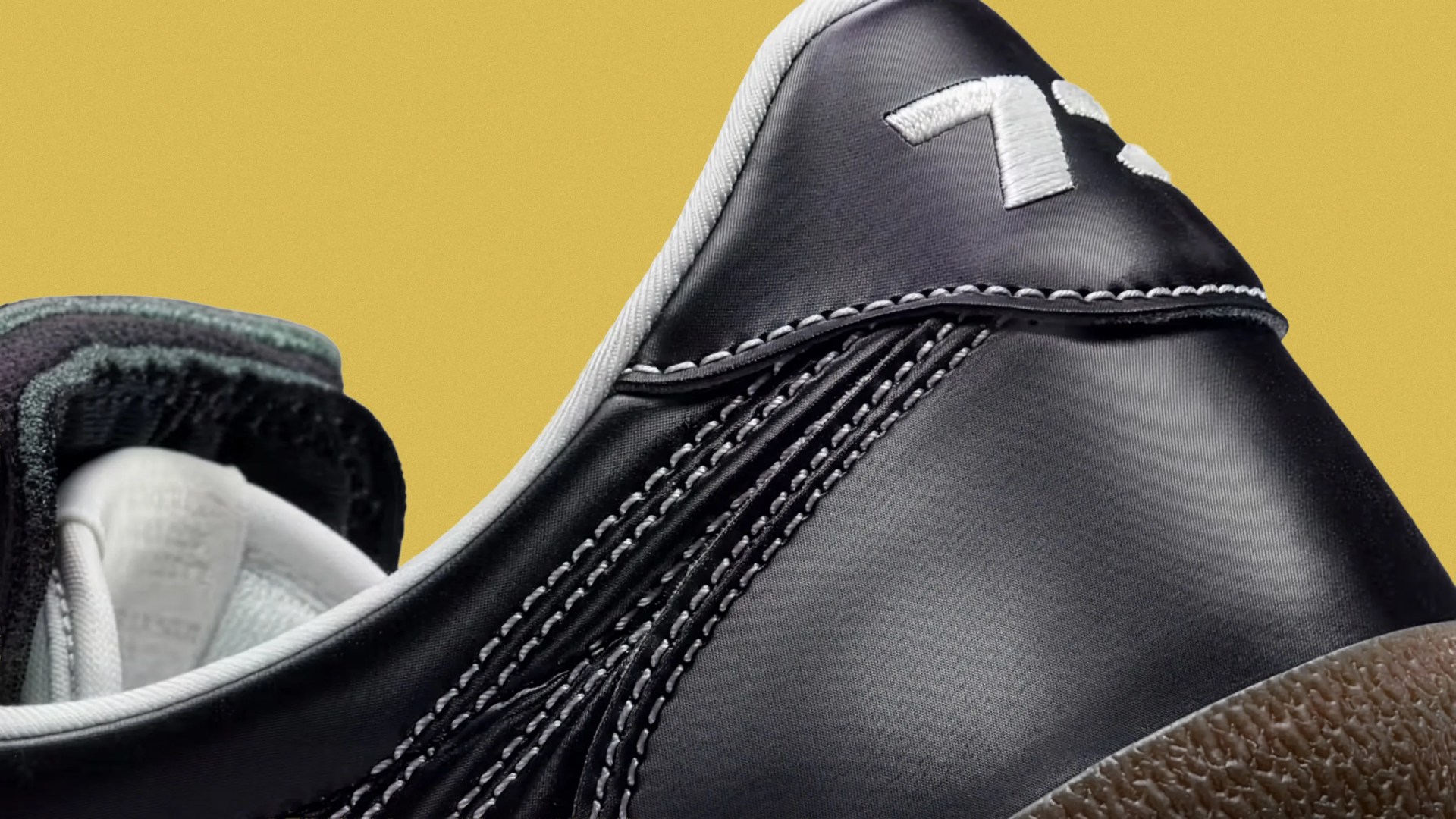 Close-up of the heel area of a black sneaker with white stitching and a brown textured sole against a yellow background.