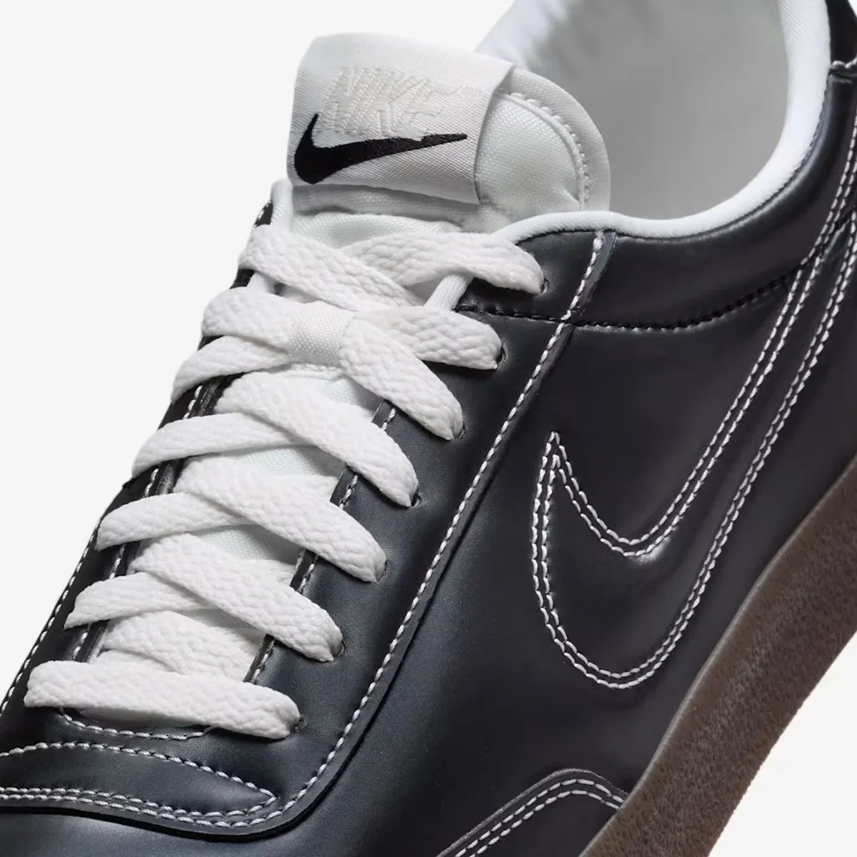 Close-up of a black Nike sneaker with white laces, white stitching, and a white Nike logo on the tongue.