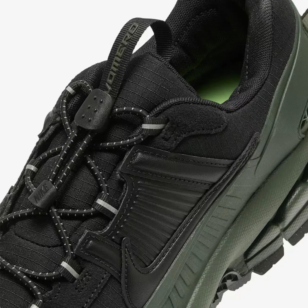 Close-up of a black and dark green Nike sneaker with reflective laces and a pull tab labeled "NIKE ACG.