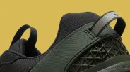 Close-up of black and dark green sneaker heel with textured fabric and geometric plastic detail against a yellow background.