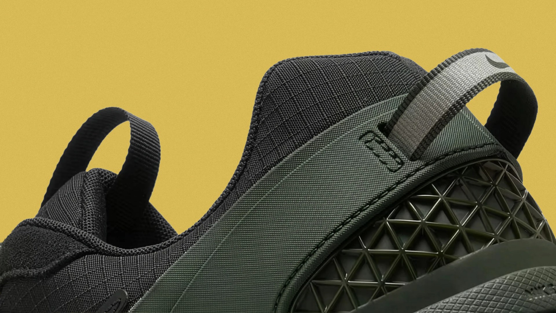 Close-up of black and dark green sneaker heel with textured fabric and geometric plastic detail against a yellow background.