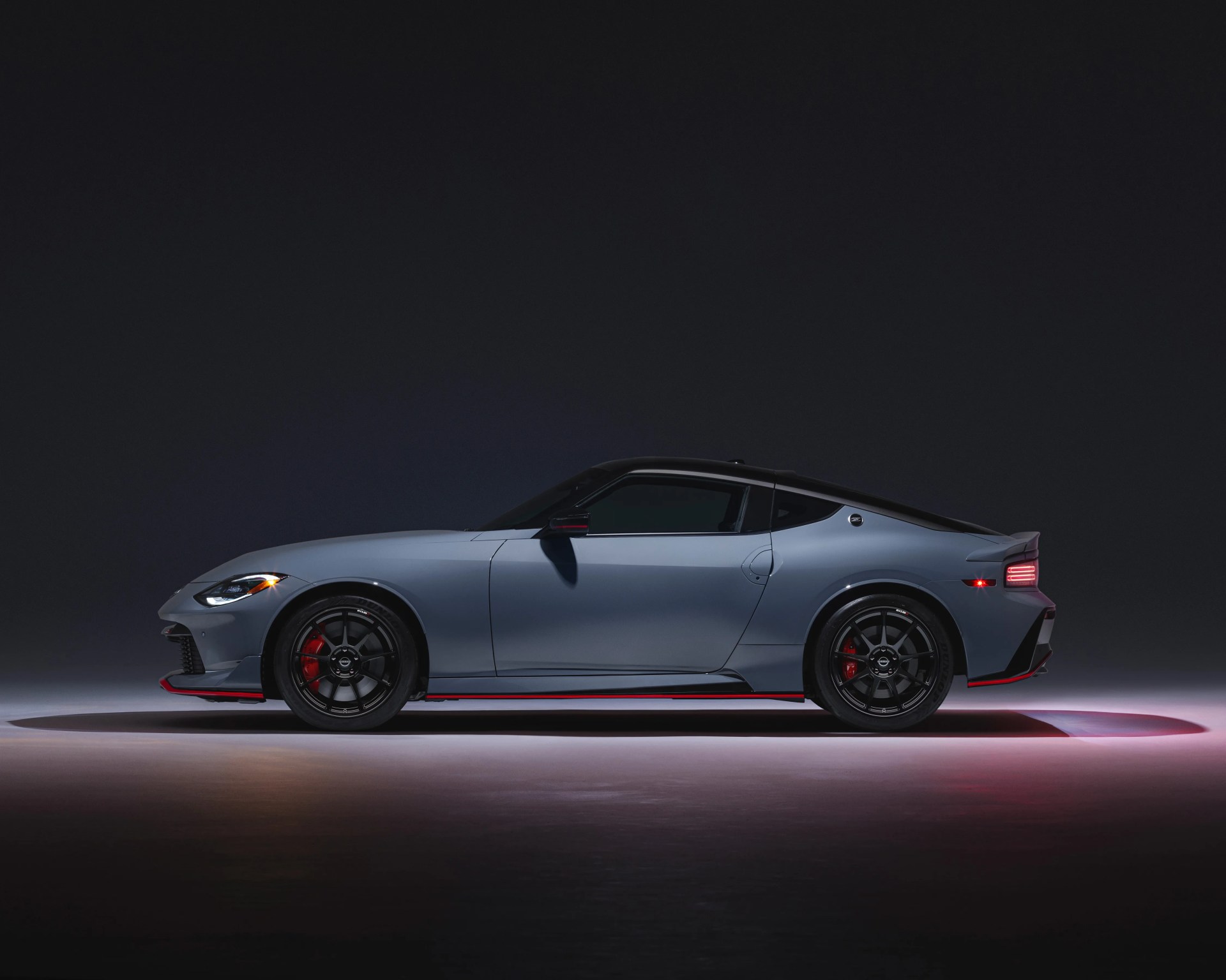Matte gray sports car with black roof, black wheels, and red accents on a dark background.