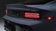 Rear view of a dark gray Nissan Z car showing illuminated red taillights and a rear spoiler.