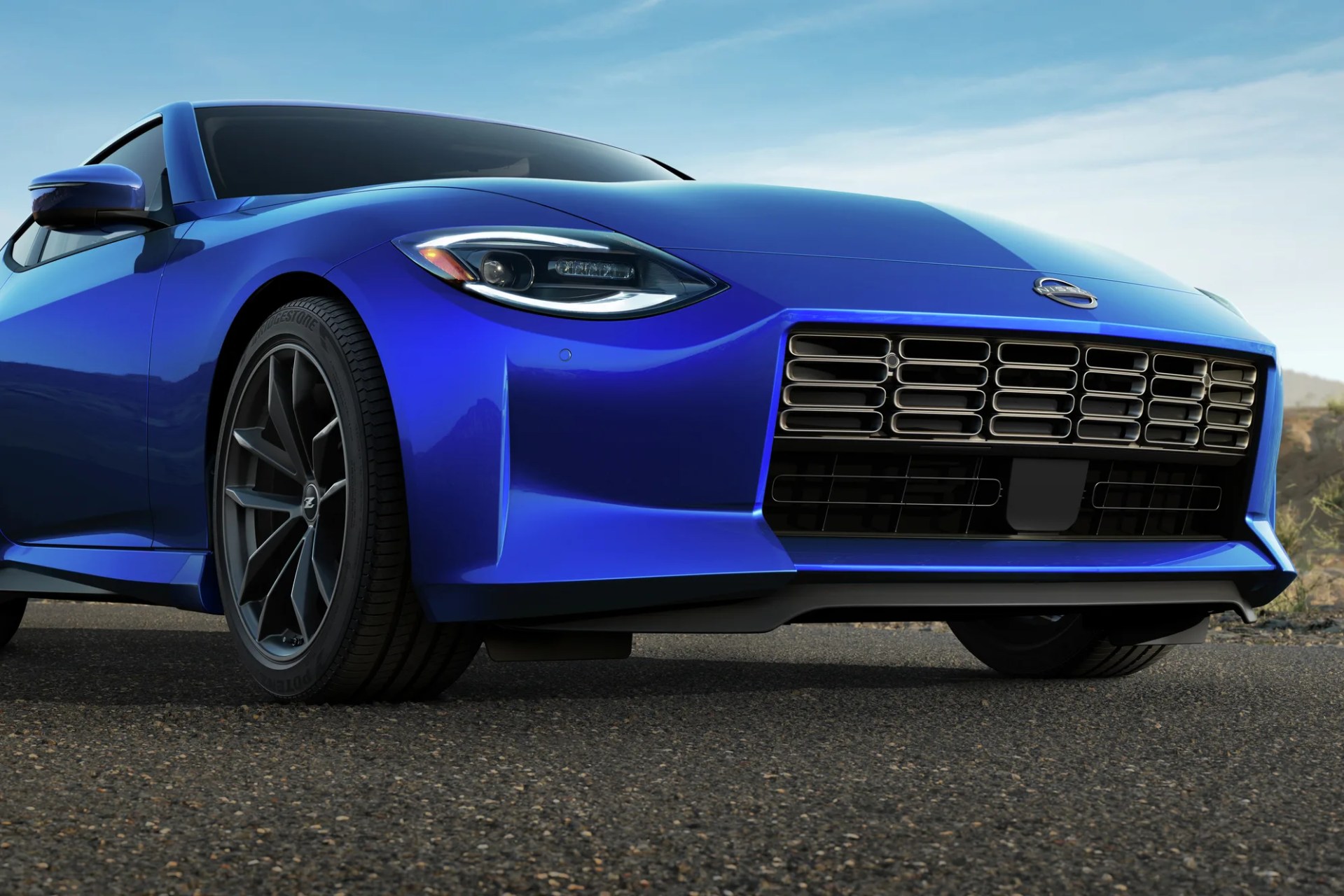Blue sports car front with black grille and dark alloy wheels on asphalt road.