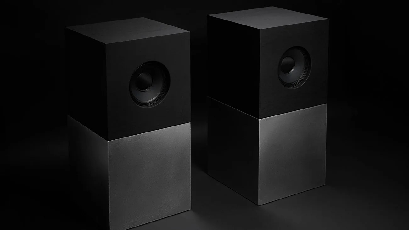 Pair of modern black and gray rectangular speakers with a single circular driver on the upper half.