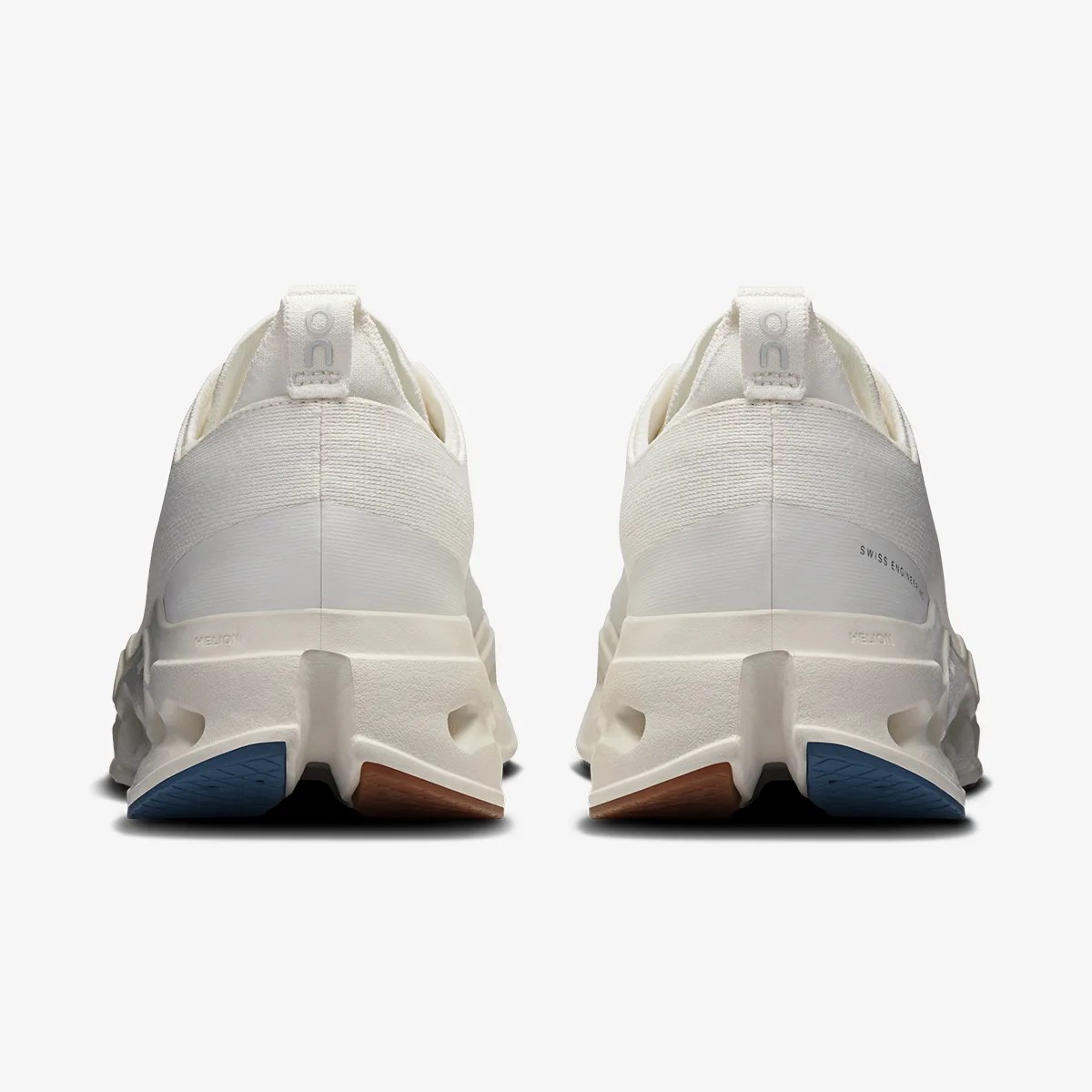 Pair of off-white athletic shoes with textured soles and blue and brown rubber accents on the heels.