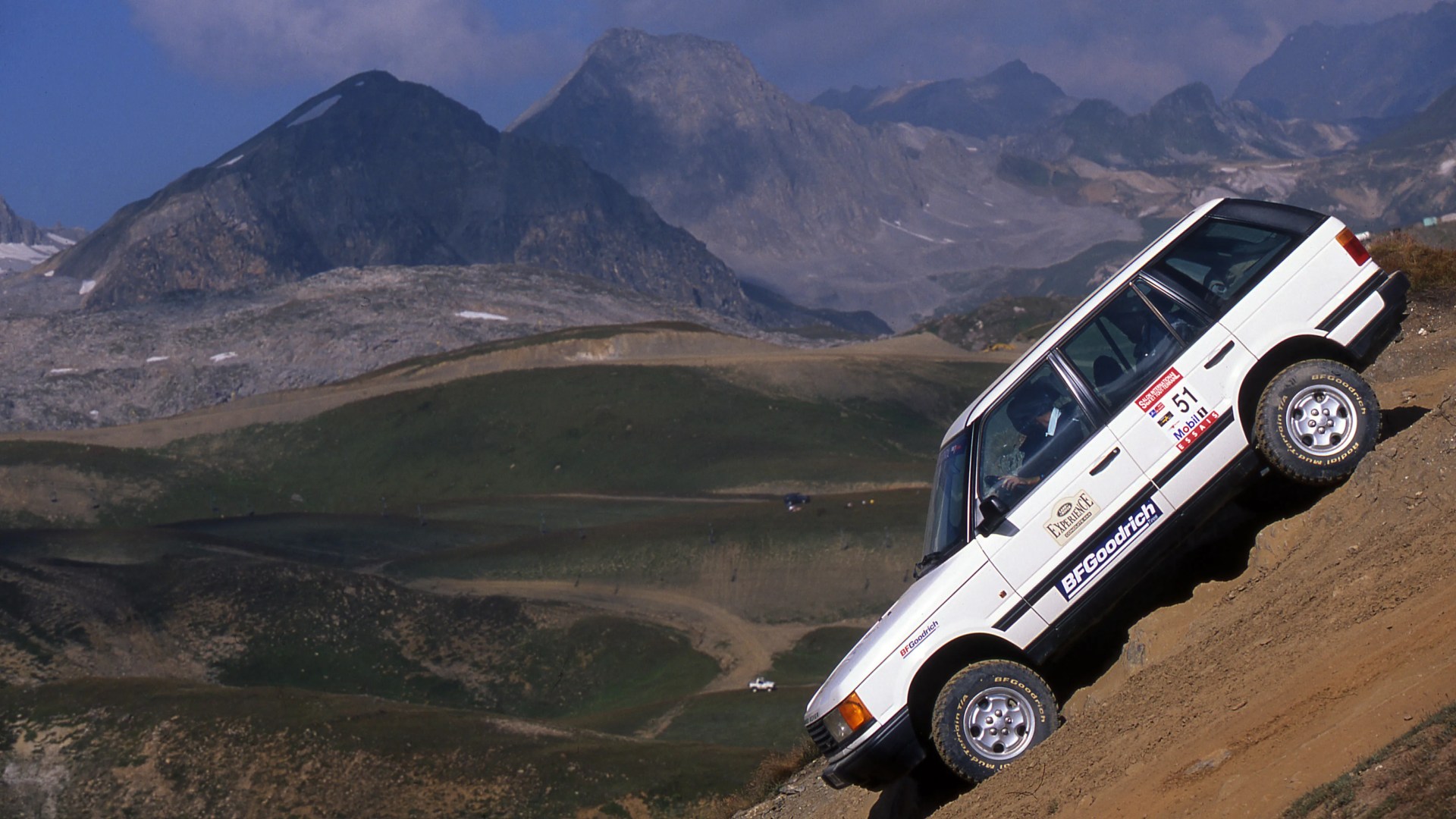 White off-road SUV with BFGoodrich tires climbing a steep dirt hill in a mountainous landscape.