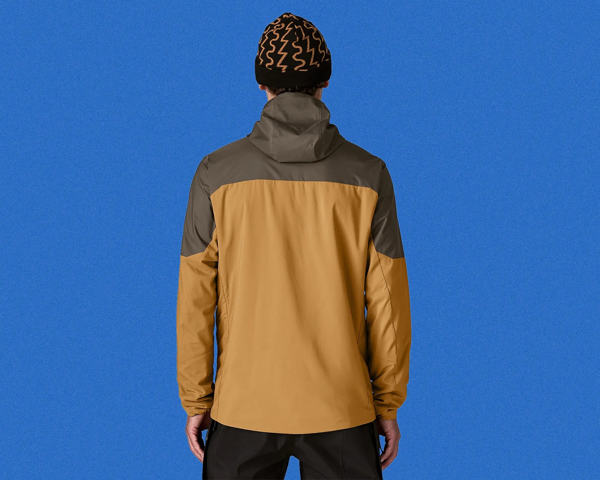 Man wearing a two-tone brown and olive hooded jacket, viewed from the back against a blue background.