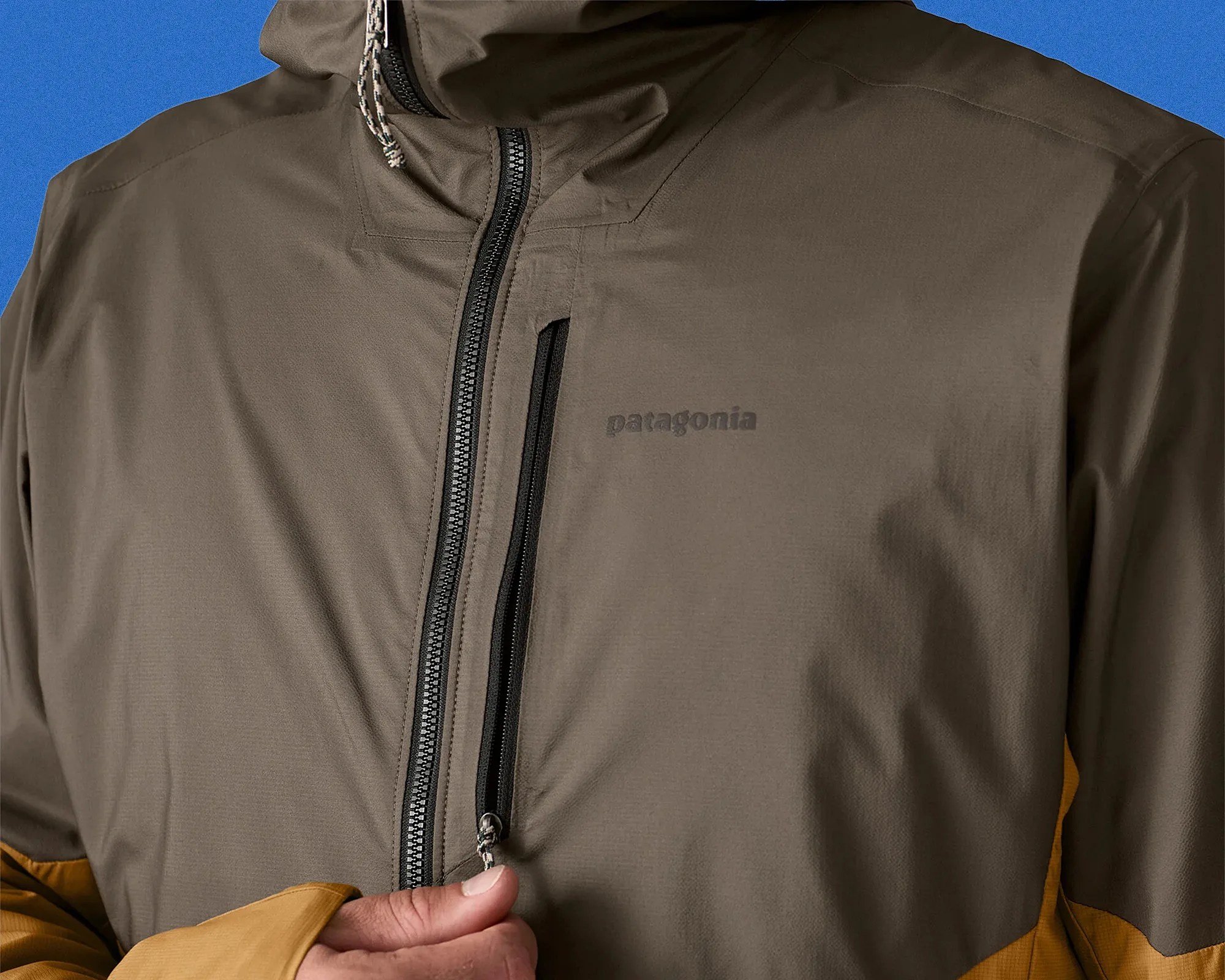 Close-up of a brown Patagonia jacket with a vertical chest zipper pocket and a black main zipper, worn by a person.