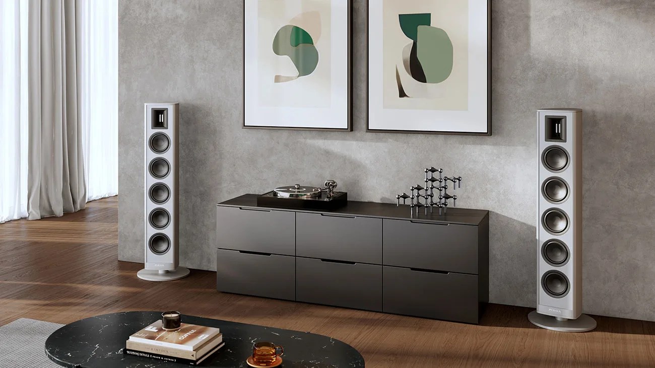 Pair of tall silver floor-standing speakers with multiple drivers flanking a black low cabinet with a turntable and decorative sculpture.