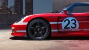 Red Porsche race car front side with white racing stripes, number 23 decal, and black five-spoke wheel.