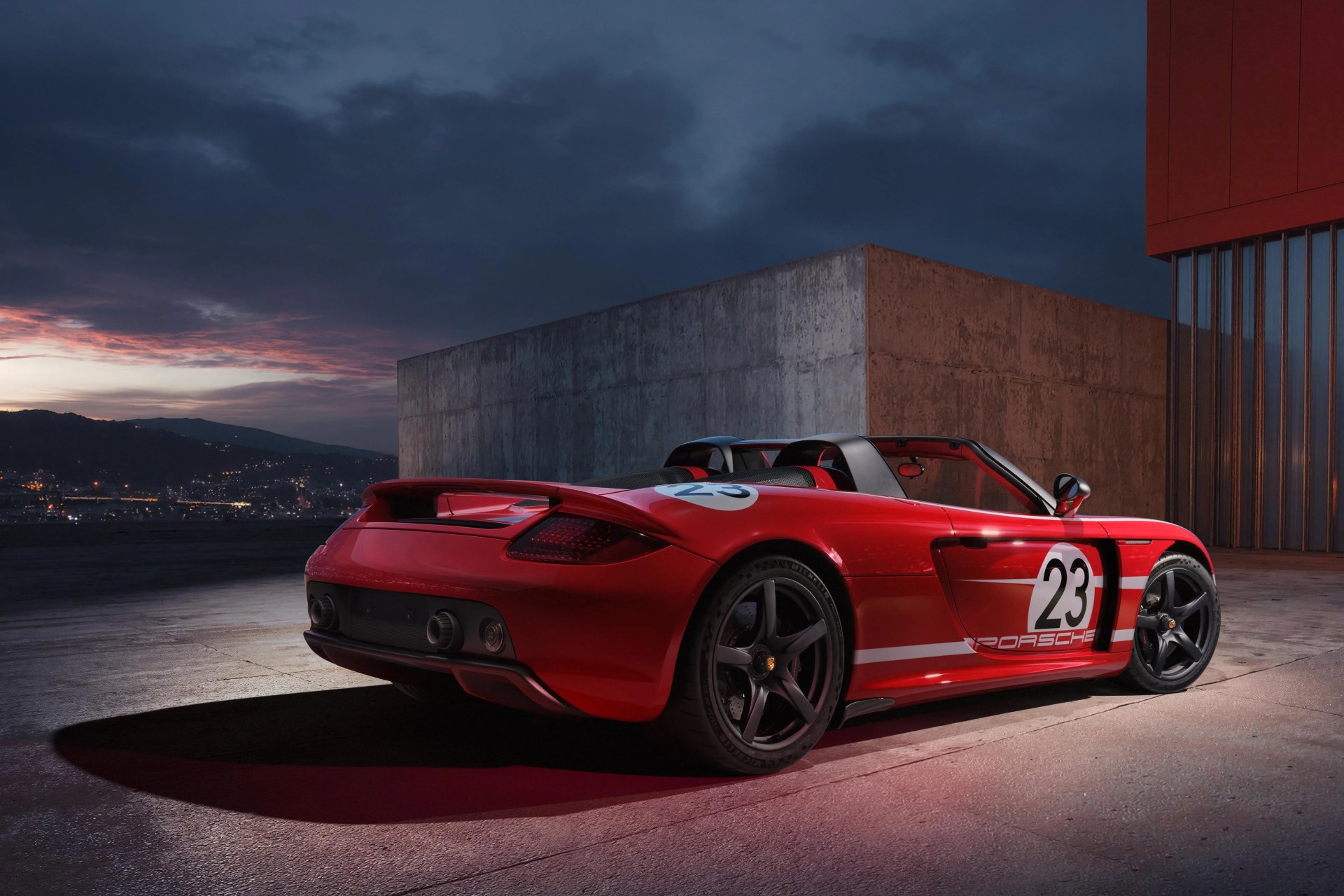 Red Porsche convertible sports car with number 23 decals parked on concrete at dusk.