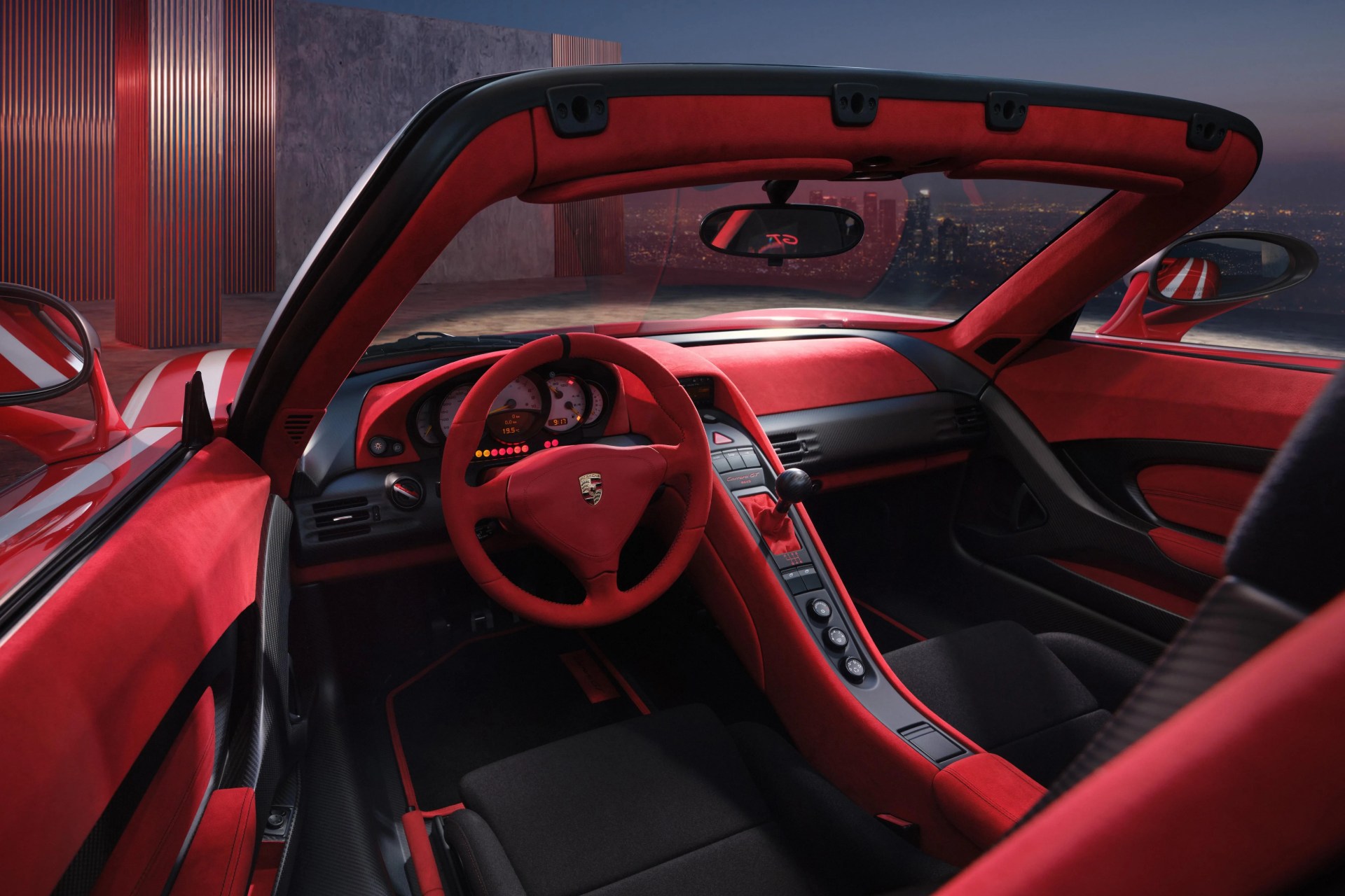 Red and black Porsche Carrera GT interior with red suede steering wheel and dashboard, and black seats.