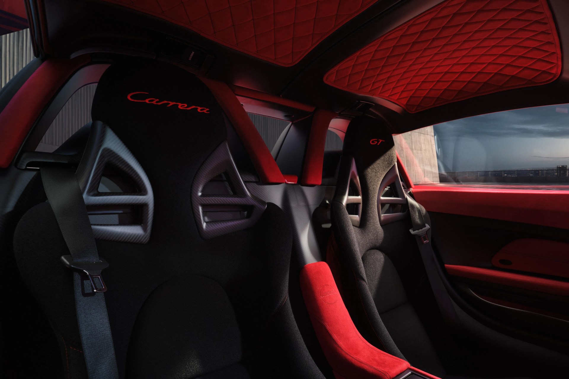 Interior of a car showing black racing seats with red "Carrera" and "GT" embroidery and red quilted ceiling panels.