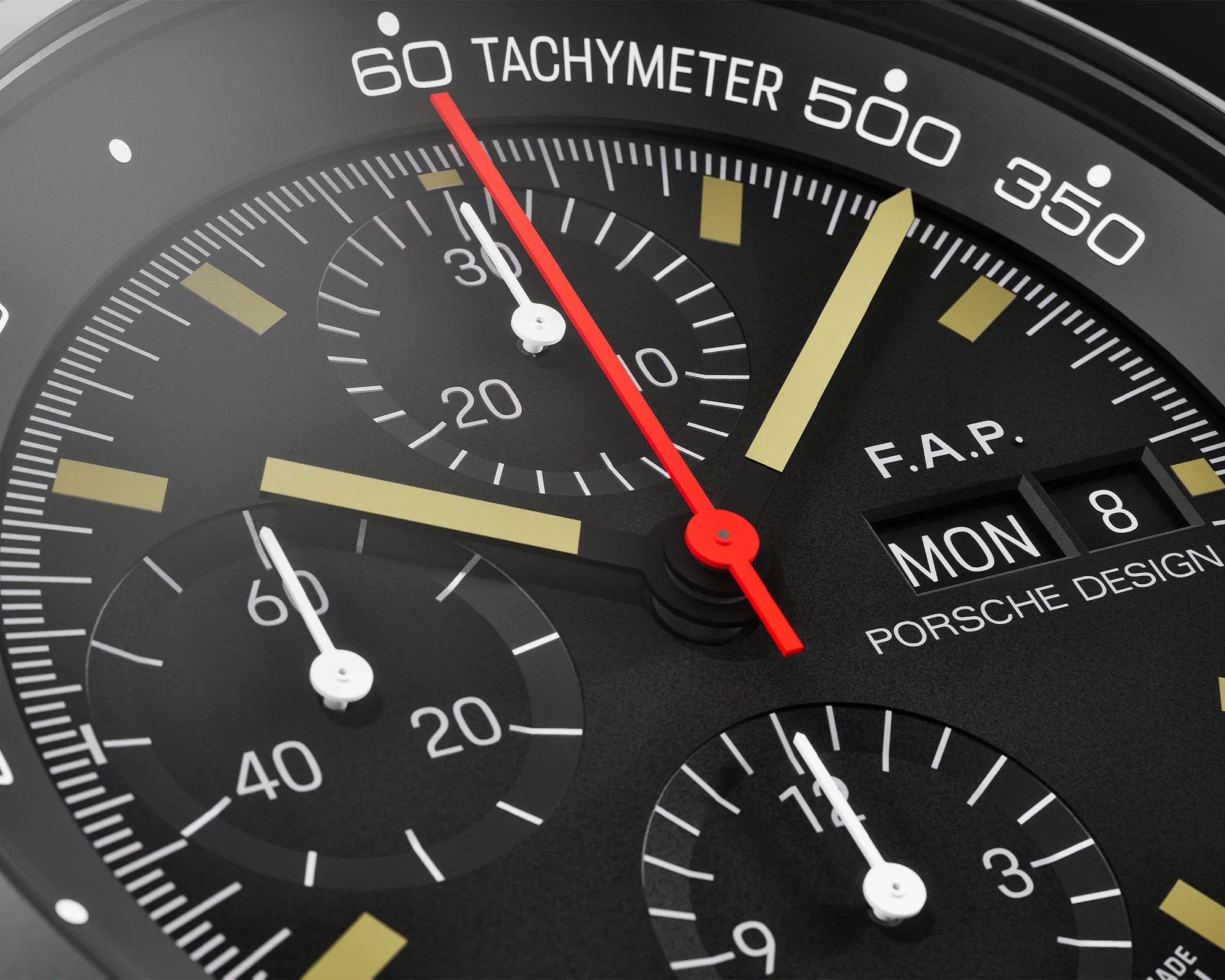 Close-up of a black Porsche Design tachymeter watch face with gold hour markers, white subdials, and red second hand.