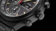 Close-up of a black Porsche Design chronograph watch face showing day and date display with red second hand.