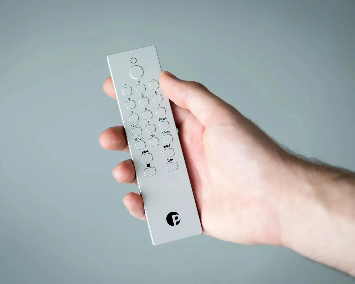 Hand holding a slim silver remote control with black buttons and a circular power button at the top.