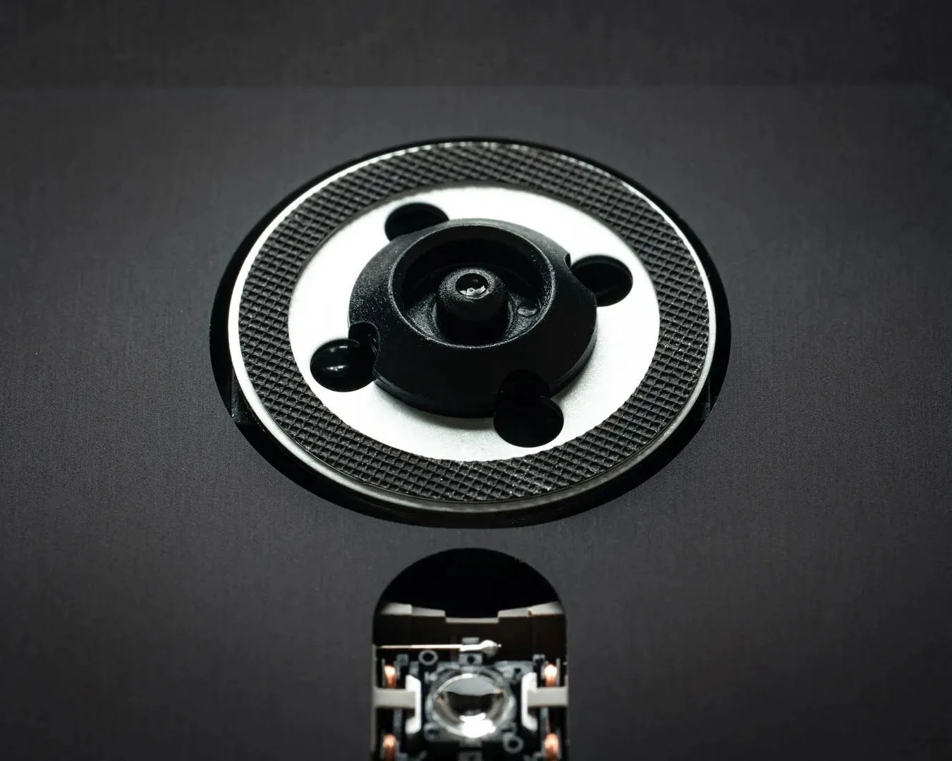 Close-up of a black and white circular mechanical component with textured edges on a dark surface.