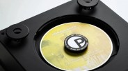Close-up of a black turntable with a yellow CD labeled "Hermann Nitsch Albertina Quartett" secured by a Pro-Ject Audio Systems anti-resonance clamp.