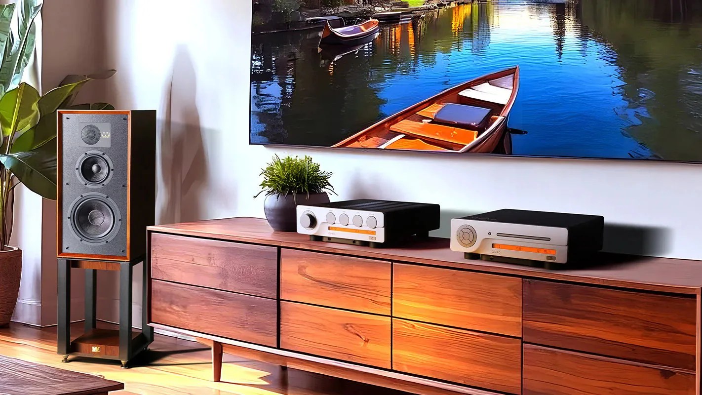 Wooden speaker on a black stand next to a wooden sideboard with audio equipment and a potted plant, under a wall-mounted TV.