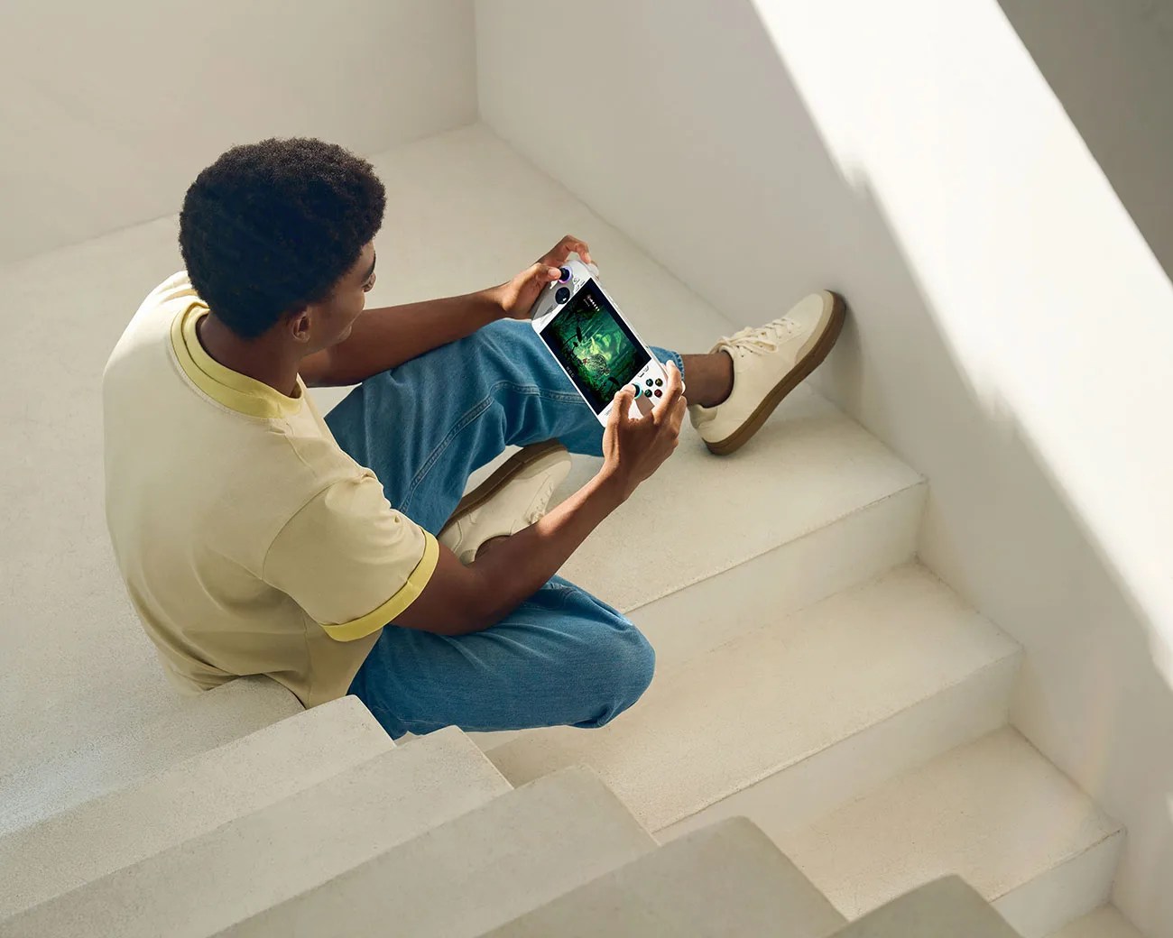 Person sitting on white stairs playing a handheld gaming device with a white body and black buttons.