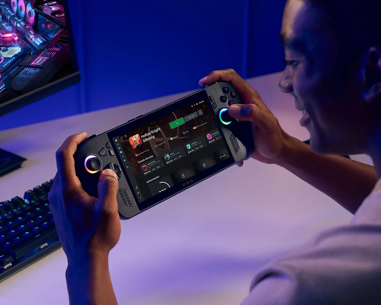 Person holding a black ROG handheld gaming device with RGB-lit controls and a game menu on screen.