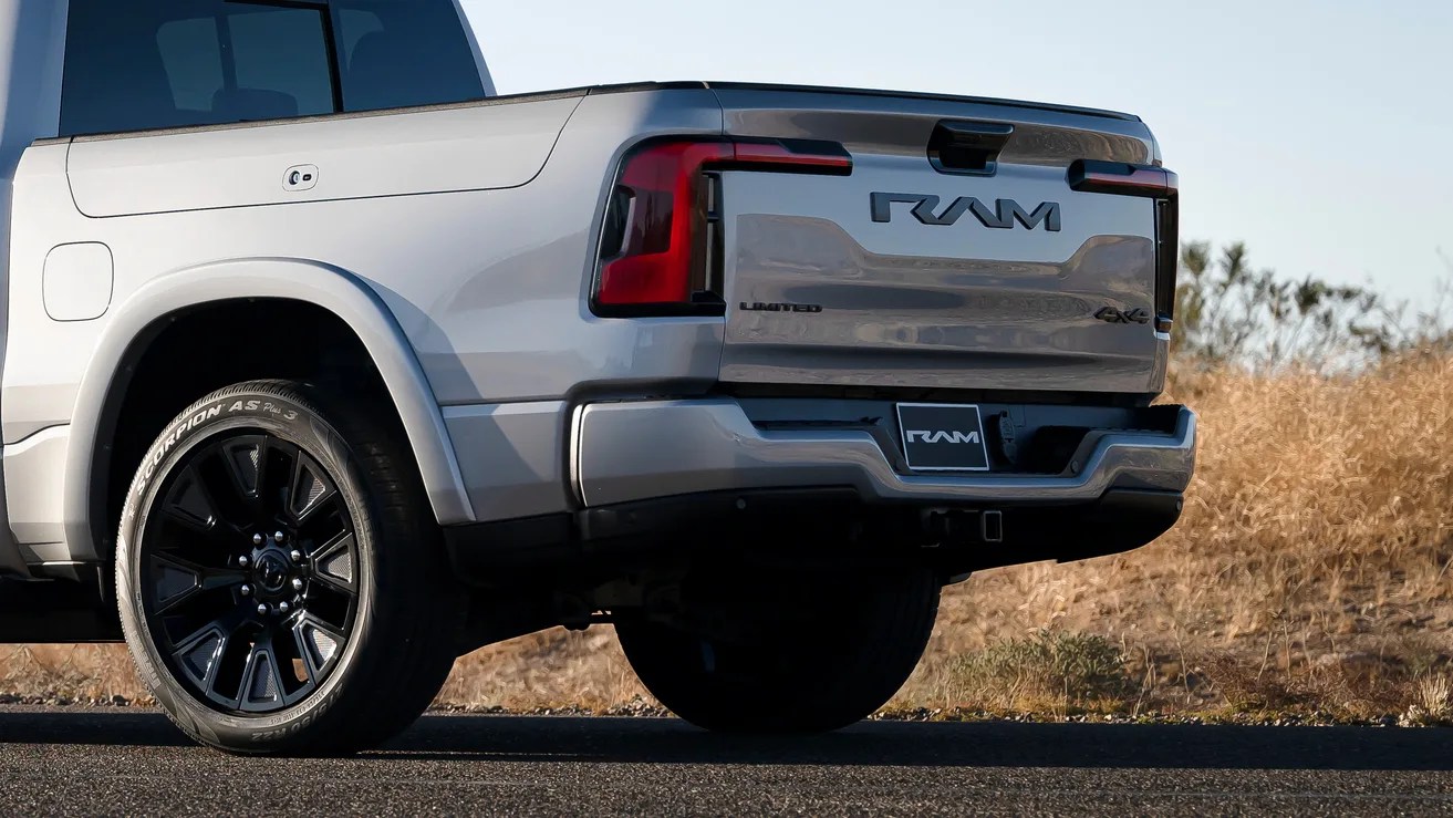 Silver RAM pickup truck rear with black wheels parked on asphalt near dry grass.