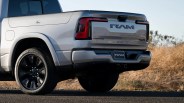 Silver RAM pickup truck rear with black wheels parked on asphalt near dry grass.