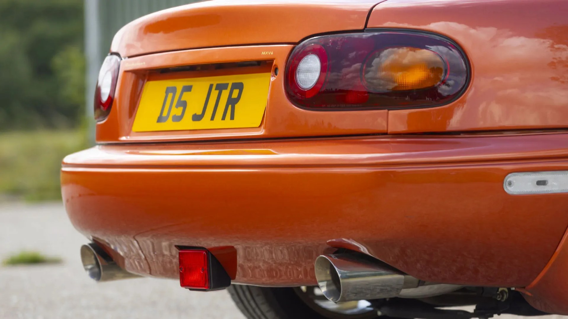 Rear view of an orange car showing dual exhaust pipes, a yellow license plate with "D5 JTR," and tail lights.