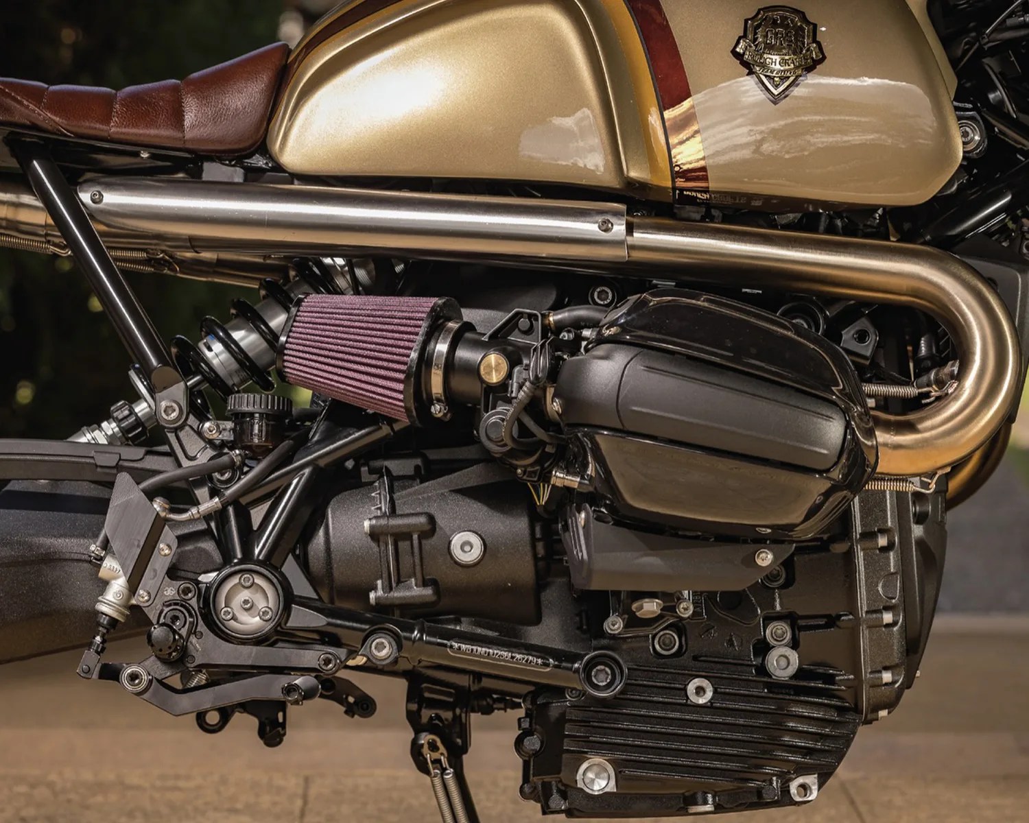 Close-up of a motorcycle engine and exhaust system with a brown leather seat and gold fuel tank.