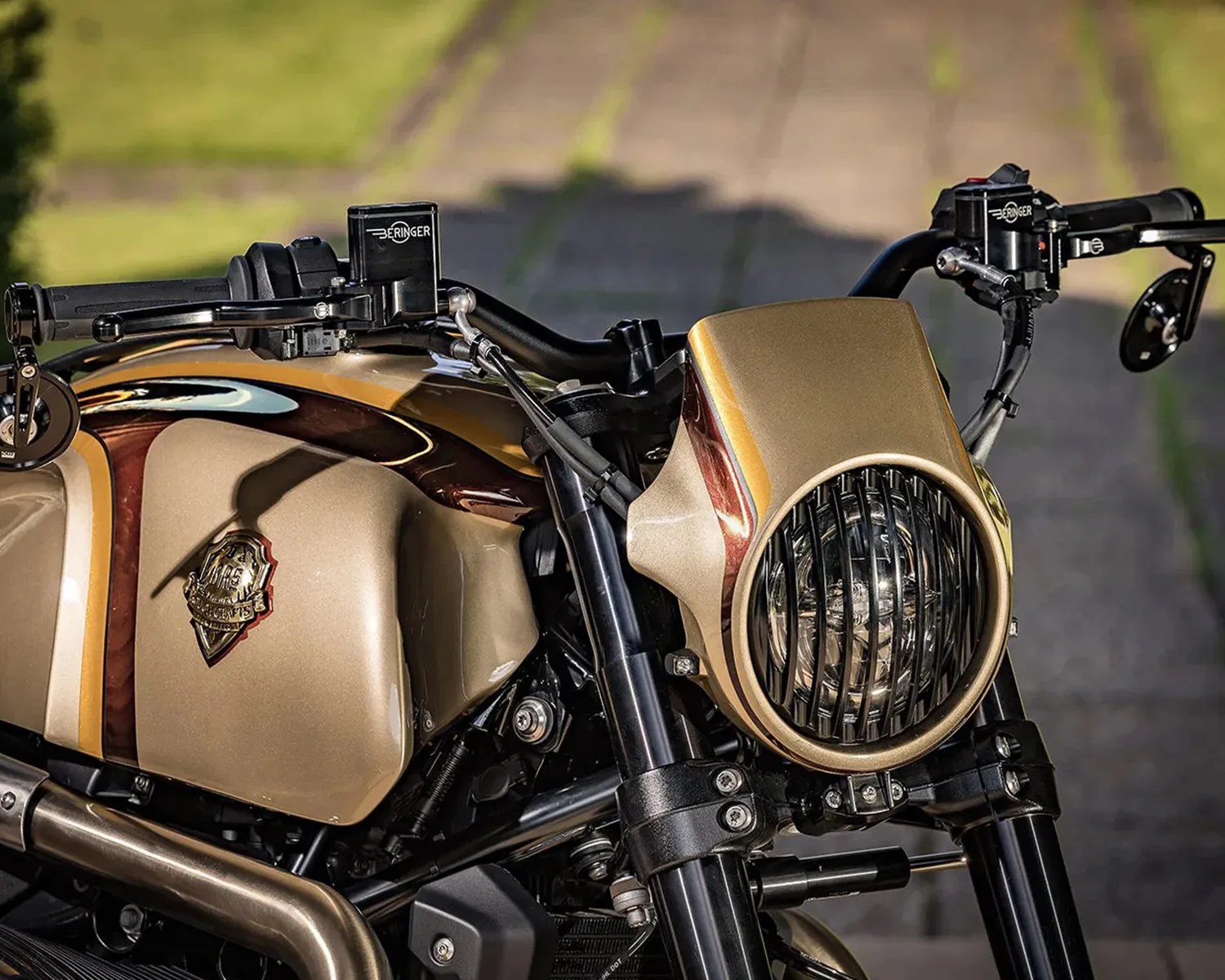 Close-up of a gold and brown motorcycle front with a round headlight protected by a black grille and Beringer brake reservoirs on the handlebars.