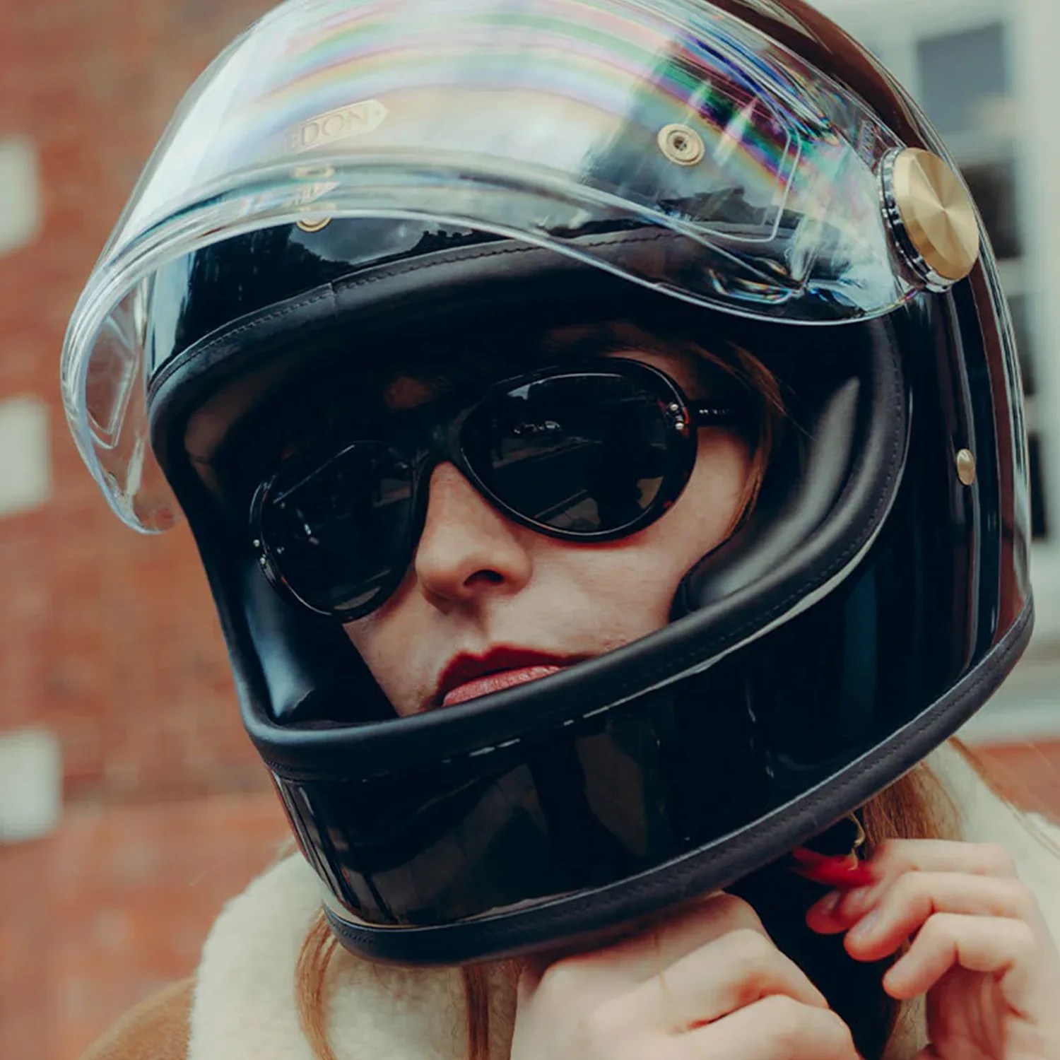 Person wearing a glossy black full-face helmet with a clear visor and black sunglasses.