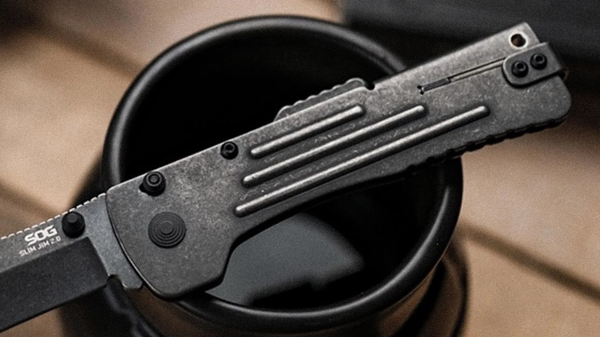 Black SOG folding knife with textured handle resting on a black cup rim.
