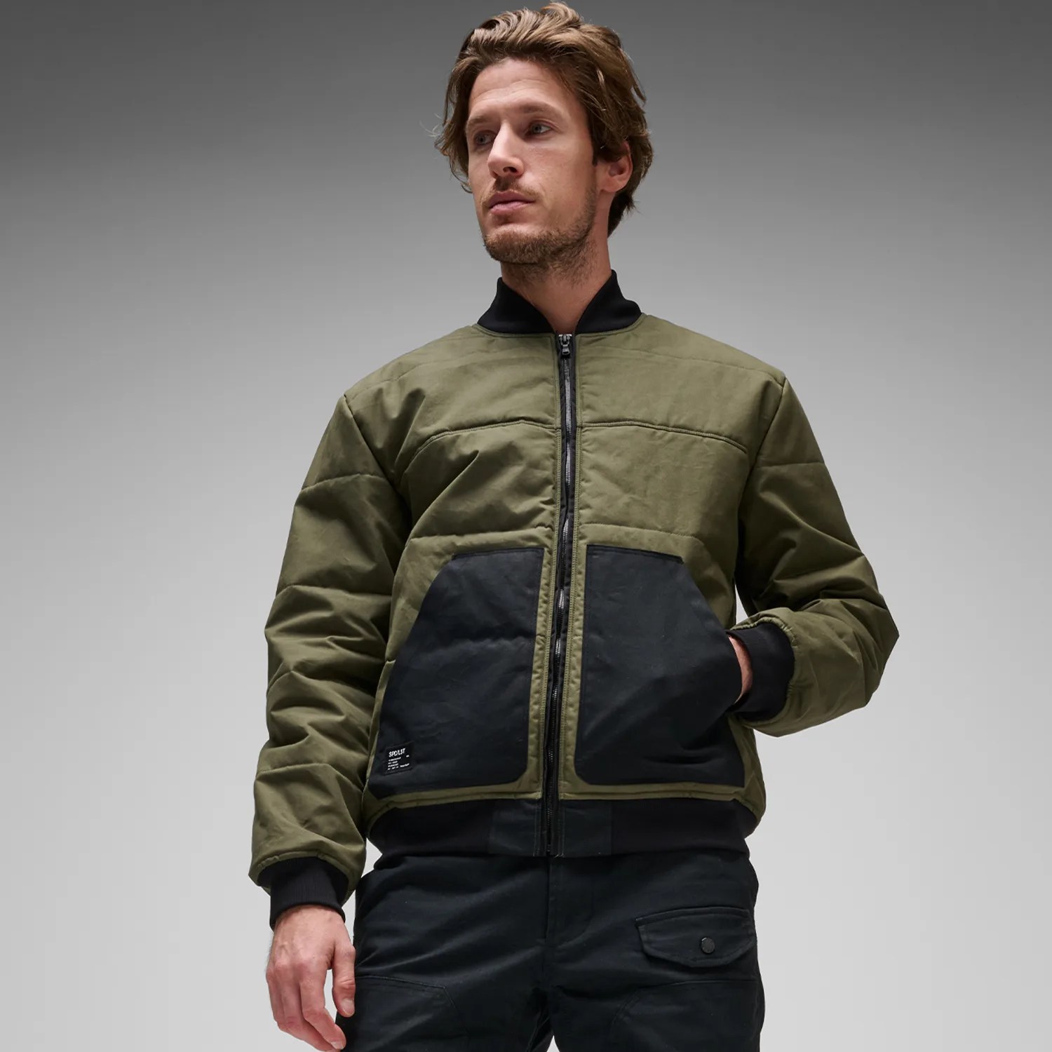 Olive green and black zip-up bomber jacket with large front pockets worn by a person.