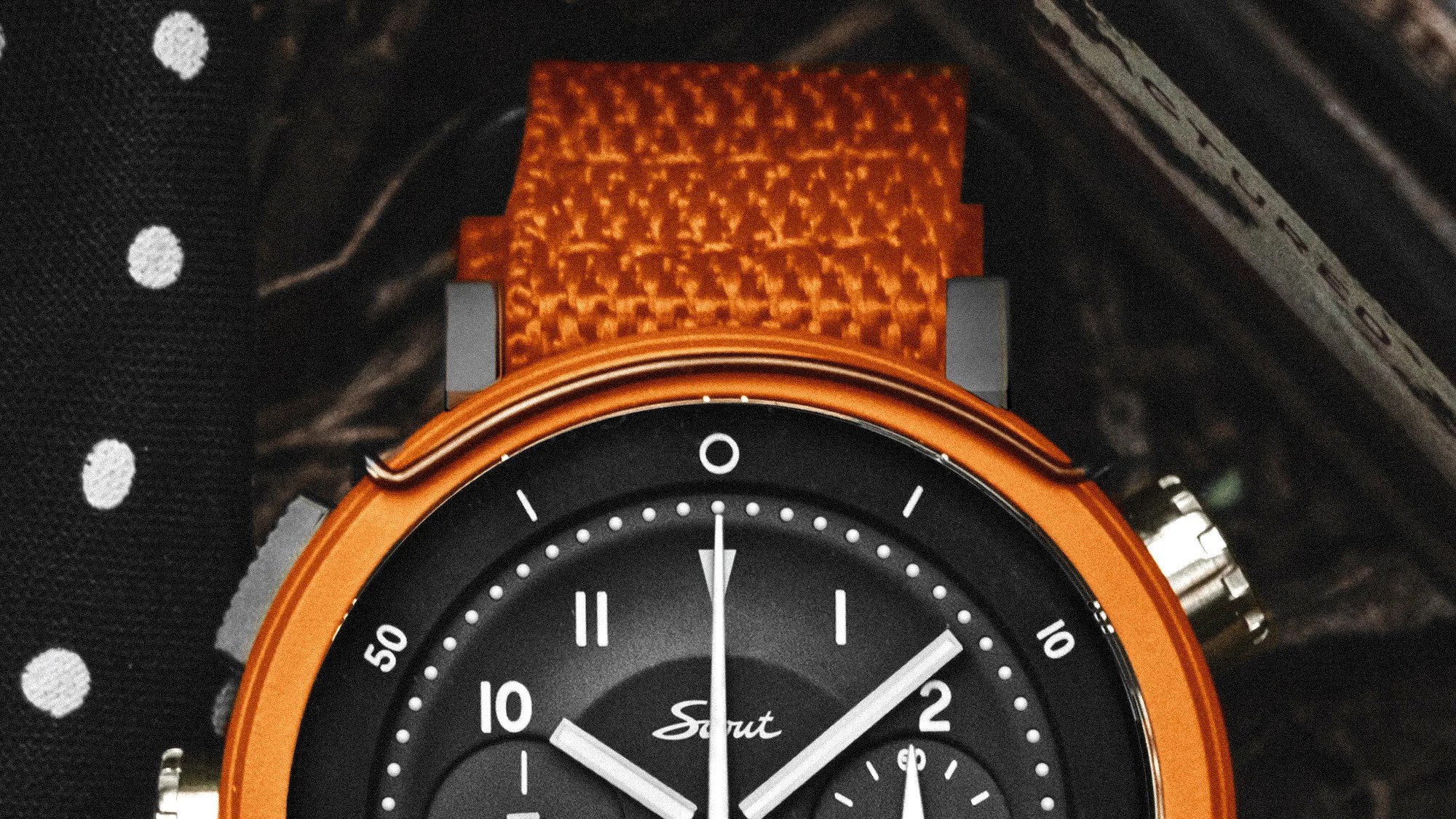 Close-up of a black watch face with white markings and hands, orange bezel, and textured orange strap.