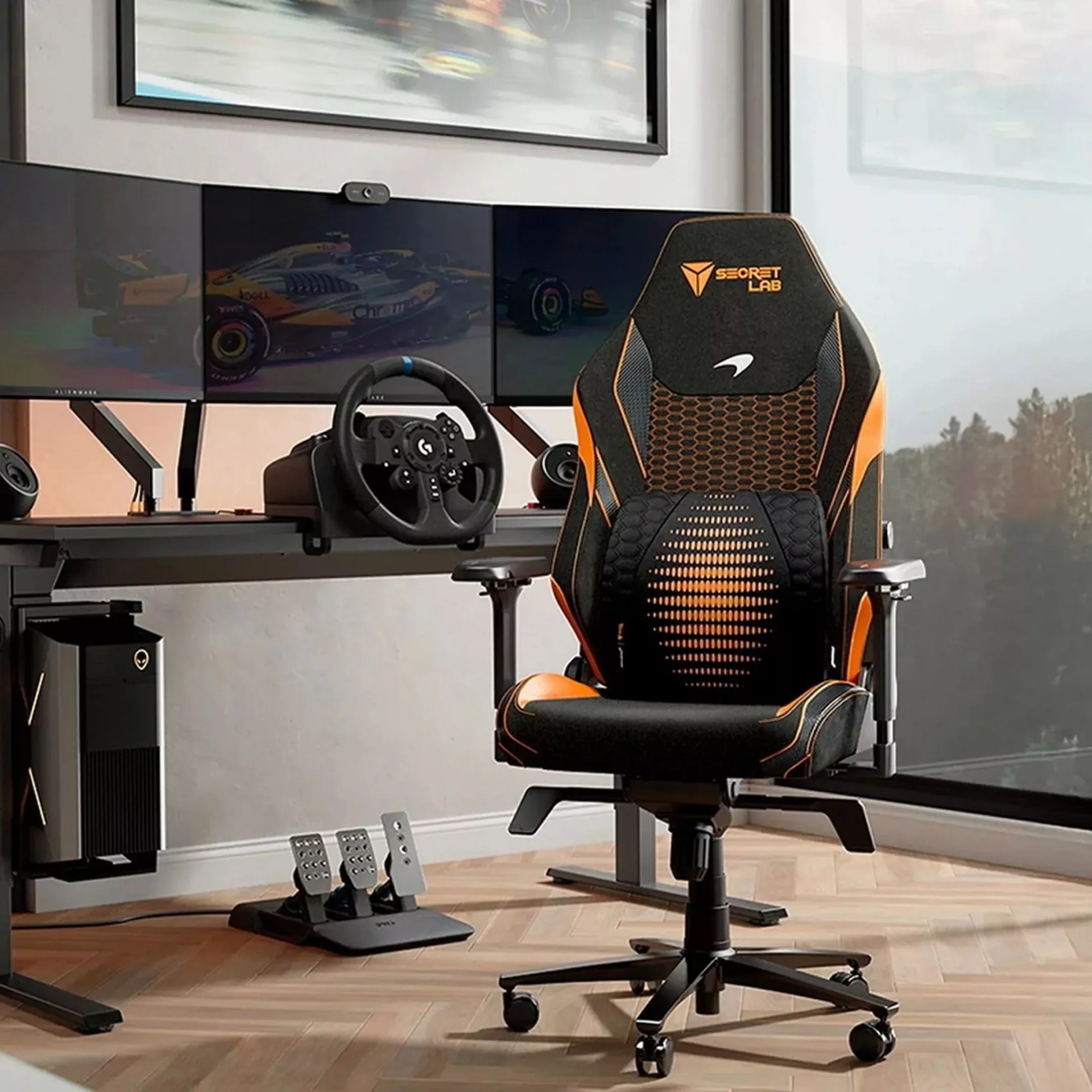 Black and orange Secretlab gaming chair with mesh backrest in front of a racing simulator setup with three monitors and a steering wheel.